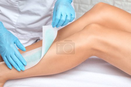 Foto de Una esteticista hace una depilación de las piernas de una mujer en un salón de belleza. Cosmetología estética femenina. - Imagen libre de derechos