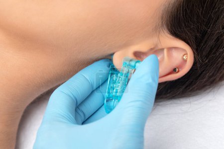 Eine Kosmetikerin macht in einem Schönheitssalon mit einem Einmalgerät eine Punktion des Ohrläppchens. Ohrenpiercing