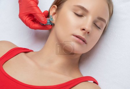 Un esteticista hace un pinchazo del lóbulo de la oreja con un dispositivo desechable en un salón de belleza. Piercing de oído