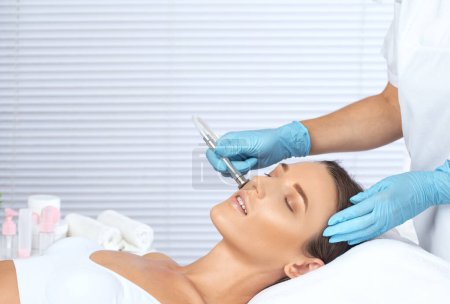 Téléchargez les photos : Cosmetologue fait procédure microdermabrasion sur le visage contre l'acné et les points noirs. Cosmétologie féminine dans le salon de beauté. - en image libre de droit