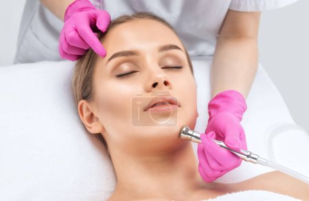 Photo for The cosmetologist makes the procedure Microdermabrasion of the face skin of a beautiful girl in a beauty salon.Cosmetology and professional skin care. - Royalty Free Image