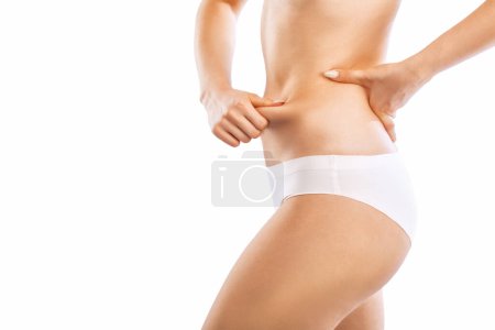 Foto de La chica tira de la piel en el abdomen, mostrando la grasa corporal. Tratamiento y eliminación del exceso de peso, depósito de grasa subcutánea. - Imagen libre de derechos