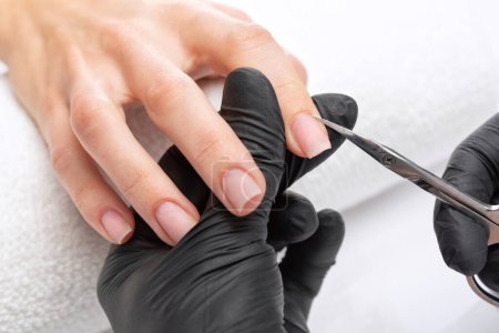A manicurist removes cuticles during a nail extension procedure in a beauty salon. Professional hand care.
