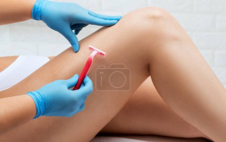 beautician shaves the hairs on the leg of a woman in a beauty salon. Removal of unwanted body hair. Elos epilation hair removal procedure on a womans body.