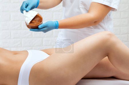Téléchargez les photos : L'esthéticienne effectue un peeling cosmétique sur les cuisses d'une femme. Procédures de spa dans un salon de beauté. - en image libre de droit