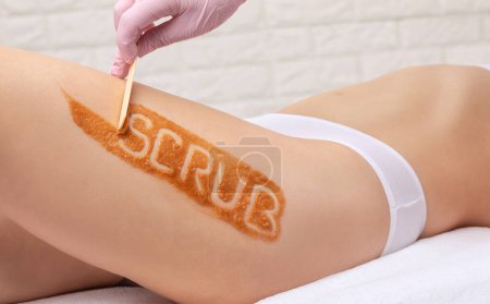 Téléchargez les photos : L'esthéticienne effectue un peeling cosmétique sur les cuisses d'une femme. Procédures de spa dans un salon de beauté. - en image libre de droit
