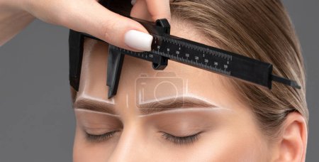 Foto de El maquillador hace las marcas con el lápiz blanco para las cejas y pinta las cejas. Maquillaje profesional y cuidado facial. - Imagen libre de derechos
