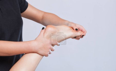 Foto de Un médico ortopédico masajea el pie y la parte inferior de la pierna del paciente después de una lesión Esguince de tobillo en la clínica.Concepto de cosmetología y masaje. - Imagen libre de derechos