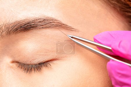 Foto de El maquillador arranca las cejas antes del procedimiento de coloración. Maquillaje profesional y cuidado de la cara. - Imagen libre de derechos