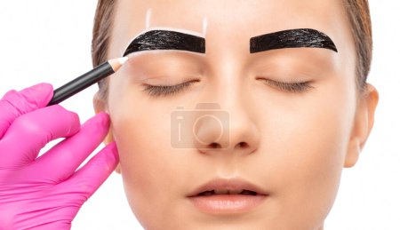 Foto de El maquillador hace marcas con un lápiz de cejas blanco y aplica pintura en las cejas. Maquillaje profesional y cuidado de la cara. - Imagen libre de derechos