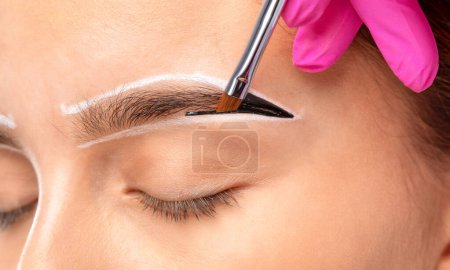 Foto de El maquillador hace marcas con un lápiz de cejas blanco y aplica pintura en las cejas. Maquillaje profesional y cuidado de la cara. - Imagen libre de derechos