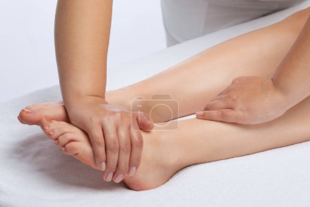 Foto de Un médico ortopédico masajea el pie y la parte inferior de la pierna del paciente después de una lesión en la clínica.Concepto de cosmetología y masaje. - Imagen libre de derechos