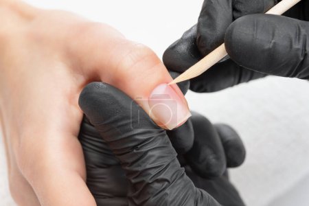 Un manucure enlève les cuticules lors d'une procédure d'extension des ongles dans un salon de beauté. Soins des mains professionnels.