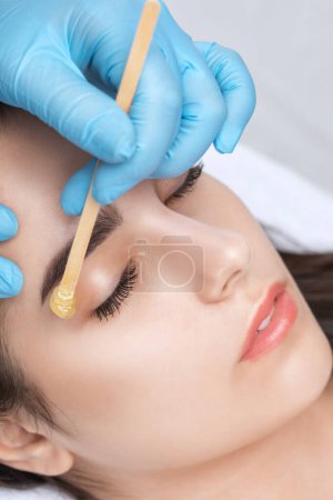 Makeup artist does facial hair removal procedure. Beautiful girl having Permanent Make-up on her Eyebrows. The make-up artist does Long-lasting styling of the eyebrows