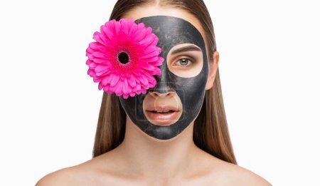 Le cosmétologue fait la procédure pour nettoyer la peau de l'acné à une belle fille aux yeux bruns dans un salon de beauté. Cosmétologie du matériel. Elle tient une fleur rose près de son visage.