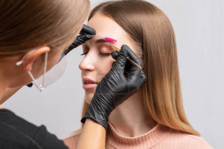Foto de Maquillaje artista arranca las cejas antes de teñir en un salón de belleza. Maquillaje profesional y cuidado cosmético de la piel. - Imagen libre de derechos