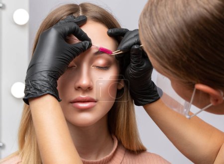 Foto de Maquillaje artista arranca las cejas antes de teñir en un salón de belleza. Maquillaje profesional y cuidado cosmético de la piel. - Imagen libre de derechos