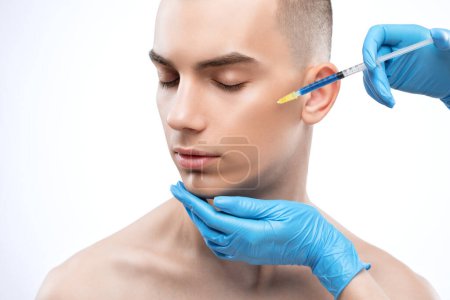 Men's cosmetology. Beautician makes a man a rejuvenation injection procedure on his face.