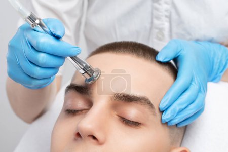 Téléchargez les photos : Un cosmétologue effectue la procédure Microdermabrasion de la peau du visage dans un salon de beauté. Cosmétologie pour hommes et soins professionnels de la peau. - en image libre de droit