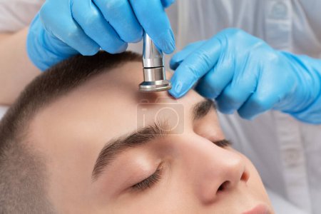 Téléchargez les photos : Un cosmétologue effectue la procédure Microdermabrasion de la peau du visage dans un salon de beauté. Cosmétologie pour hommes et soins professionnels de la peau. - en image libre de droit