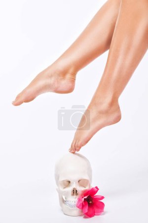 Belles jambes fines d'une femme à côté d'un crâne humain sur un fond blanc.
