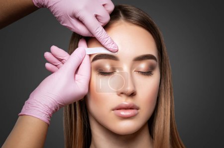 Makeup artist does facial hair removal procedure. Beautiful girl having Permanent Make-up on her Eyebrows. The make-up artist does Long-lasting styling of the eyebrows