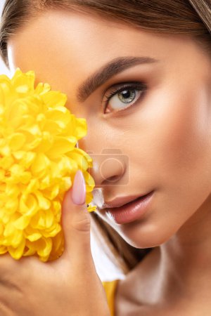 Portrait of an attractive girl with healthy clean skin and beautiful makeup, she is holding a yellow chrysanthemum. Aesthetic cosmetology and make-up concept.