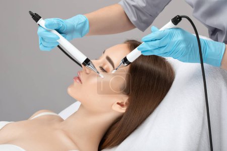 Photo for A doctor cosmetologist makes a microcurrent facial therapy to a young woman with a device in a beauty wellness salon.Cosmetology and professional skin care. - Royalty Free Image