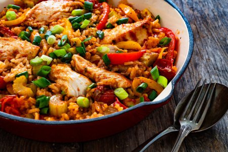 Jambalaya one pot dish - fried chicken breasts with white rice, tomatoes, bell pepper and celery on wooden table 