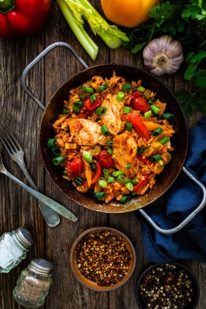 Jambalaya one pot dish - fried chicken breasts with white rice, tomatoes, bell pepper and celery on wooden table 