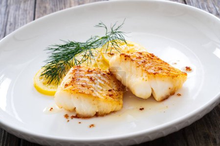  Seared cod loin and sliced lemon on wooden table 