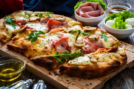 Pizza romaine au jambon, fromage mozzarella et champignons blancs sur table en bois 
