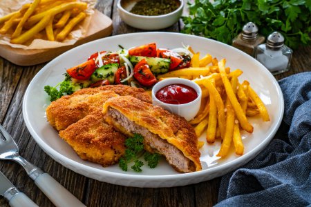 Crispy breaded fried pork loin chops with fries and fresh vegetables on wooden table 