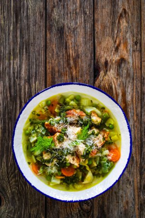 Sopa Pistou Niza - caldo con pesto de albahaca, pan, queso y verduras sobre fondo de madera en tazón blanco 