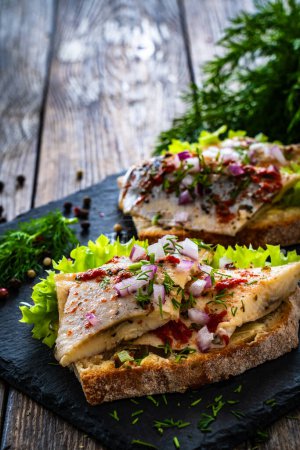  Tasty sandwiches - toasted bread with pickled herrings and red onion on wooden table 