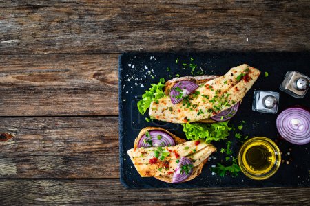 Tasty sandwiches - toasted bread with pickled herrings on and red onion on wooden table 