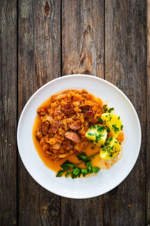 Bigos - cooked cabbage with sliced sausage and boiled potatoes on wooden table