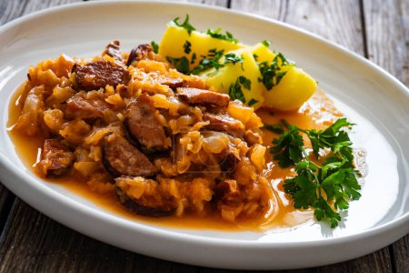 Bigos - cooked cabbage with sliced sausage and boiled potatoes on wooden table