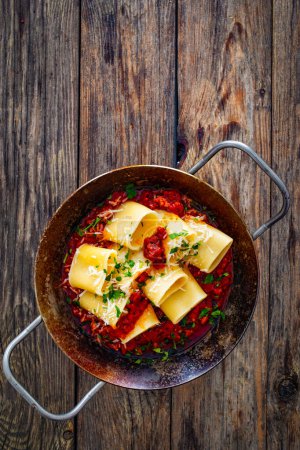 Paccheri con rag alla bolognese - noodles with bolognese sauce on frying pan on wooden table 