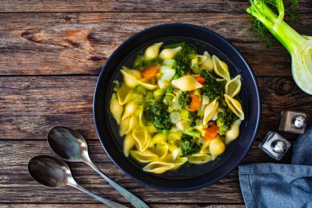 Sopa Pistou Niza - caldo con pesto de albahaca, fideos y verduras sobre fondo de madera en tazón negro