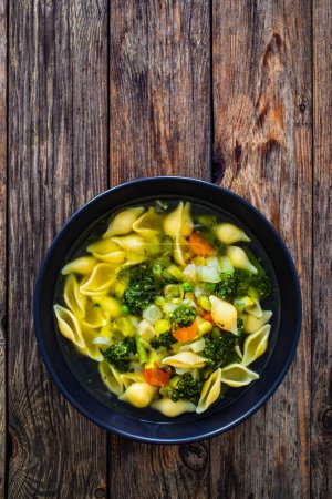 Sopa Pistou Niza - caldo con pesto de albahaca, fideos y verduras sobre fondo de madera en tazón negro