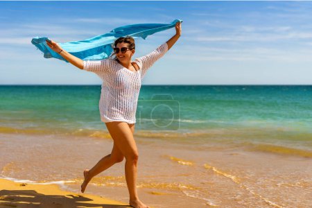 Beautiful woman walking on sunny beach holding shawl 