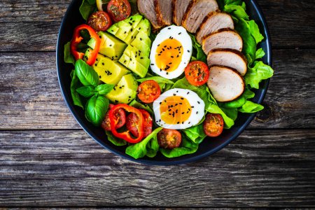 Leckerer Salat - gebratenes Kalbsrücken, Avocado, gekochte Eier und frisches Gemüse auf Holztisch 
