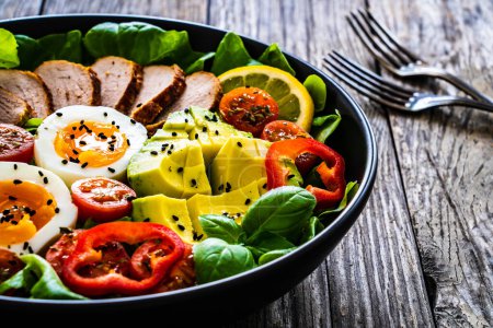 Leckerer Salat - gebratenes Kalbsrücken, Avocado, gekochte Eier und frisches Gemüse auf Holztisch 