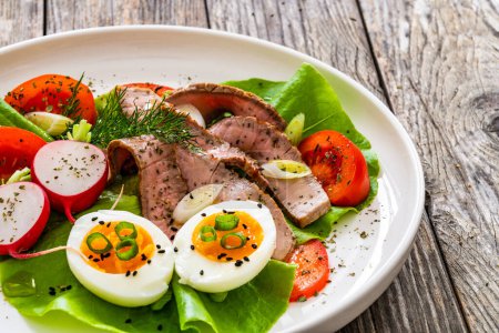 Tasty salad - roasted beef loin boiled eggs and fresh vegetables on wooden table 