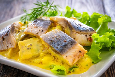 Marinated herring fillets in mustard sauce with dill and lettuce on wooden table 