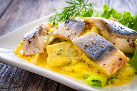 Marinated herring fillets in mustard sauce with dill and lettuce on wooden table 
