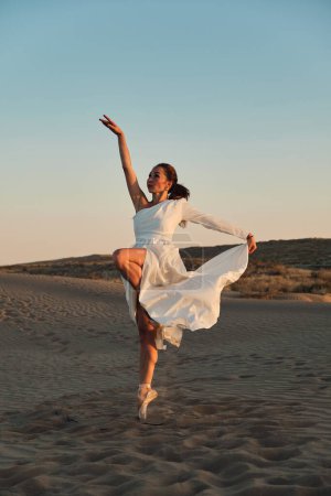 Téléchargez les photos : Une fille en robe blanche danse et pose dans le désert de sable au coucher du soleil. - en image libre de droit