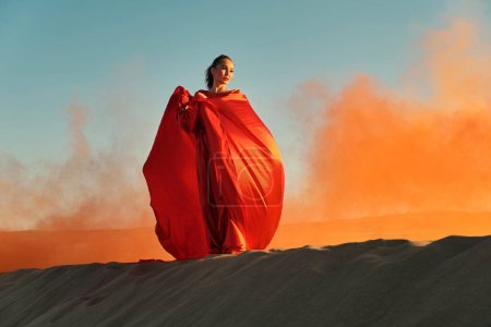 Téléchargez les photos : Femme en robe rouge dansant dans le désert au ciel bleu - en image libre de droit