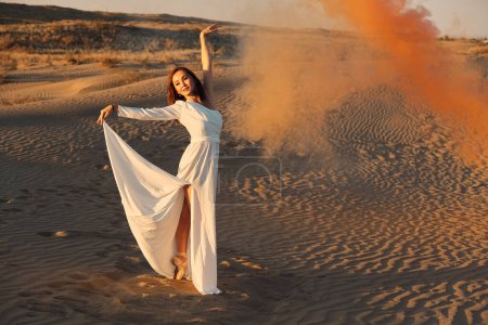 Foto de Una chica con un vestido blanco de mosca baila y posa en el desierto de arena al atardecer. - Imagen libre de derechos
